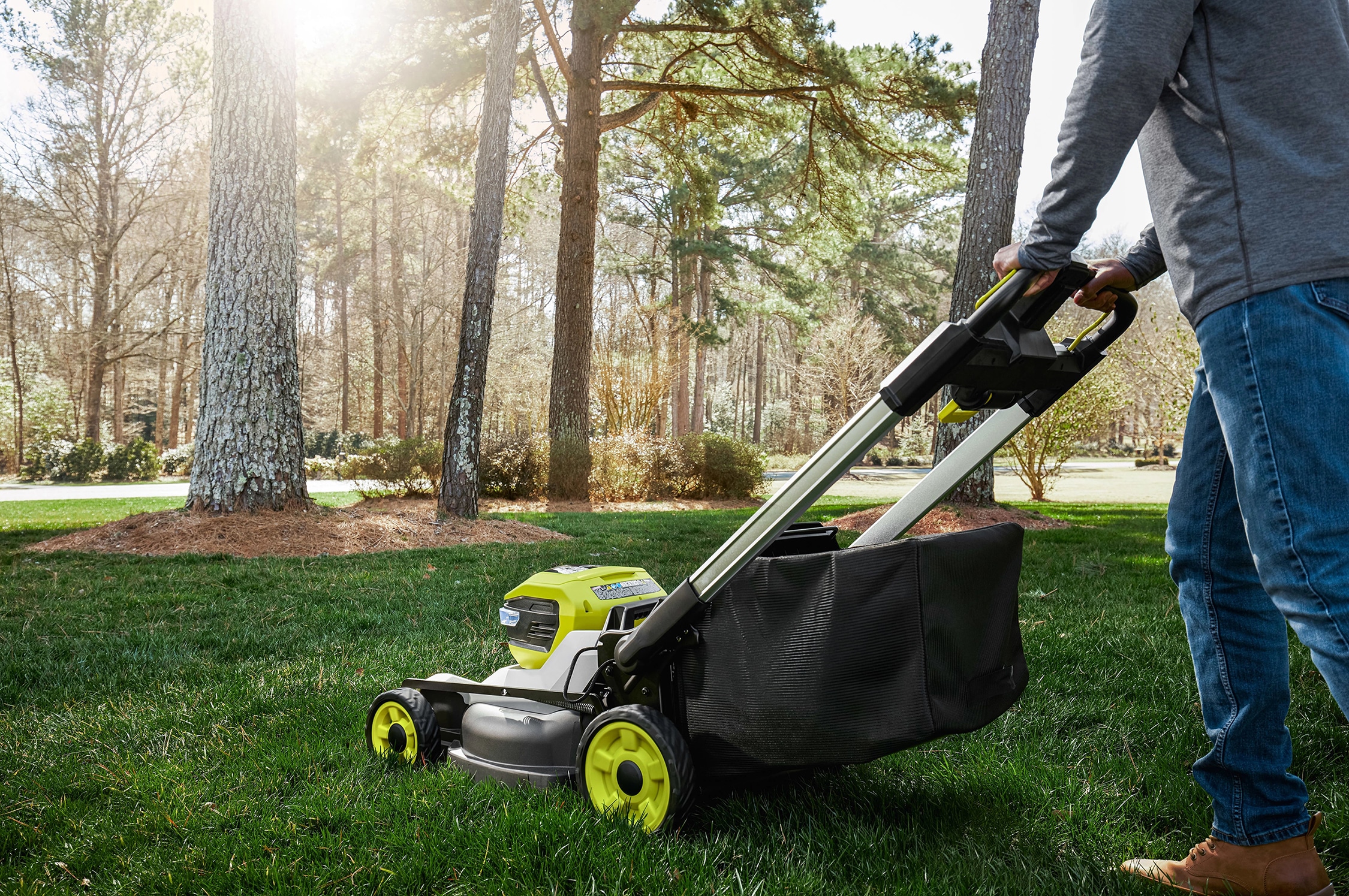 A person pushing a battery-powered Ryobi lawn mower over a green, sunlit lawn—an everyday scene that prompted a quick online search for the correct blade bolt size and led to discovering how AI-driven search can provide faster, more direct answers than traditional search engines.